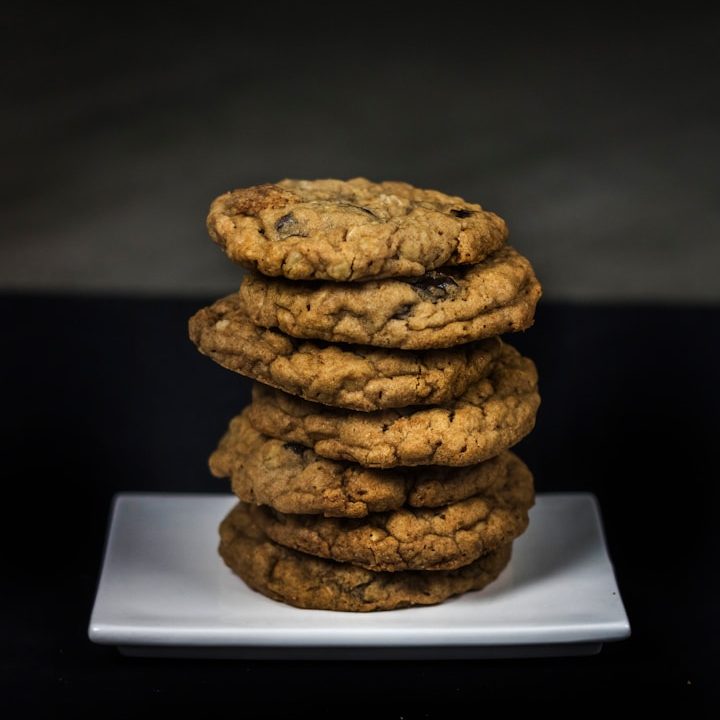 Zeven gestapelde koekjes op een wit bord tegen een donkere achtergrond.