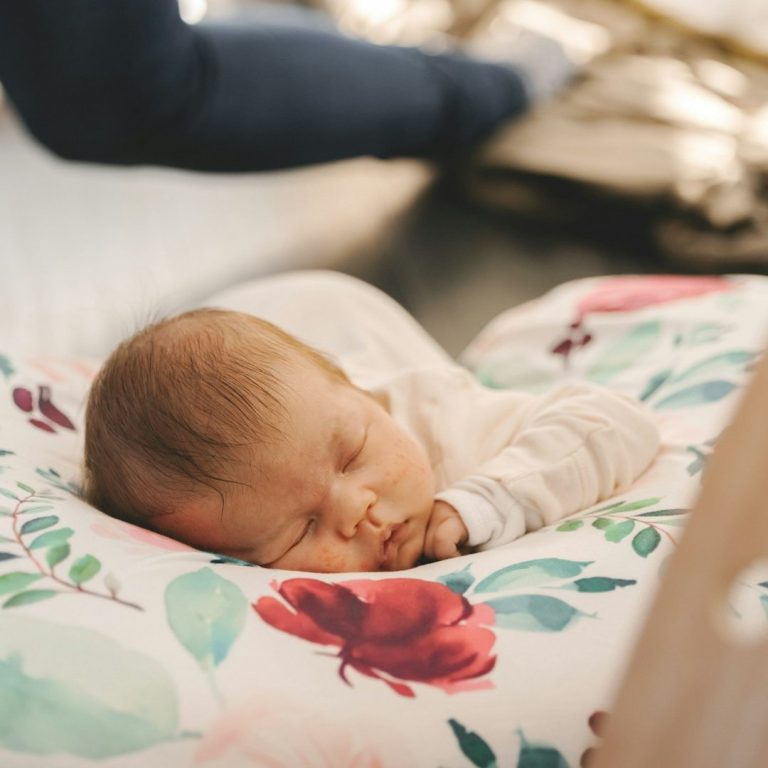 Een slapende baby op een kussen met bloemenmotief.