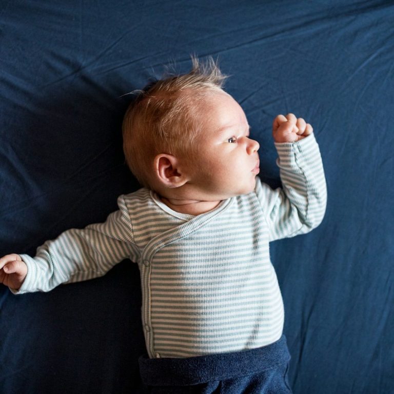 Een baby ligt op zijn rug, met een neutrale achtergrond en gestreepte kleding.