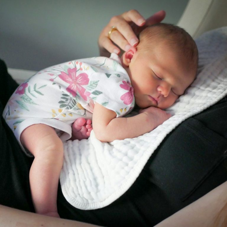 Een pasgeboren baby slaapt op de borst van een volwassene in een bloemig rompertje.