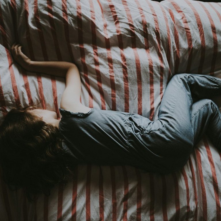 Een peuter ligt in ontspannen houding op een gestreept beddengoed.