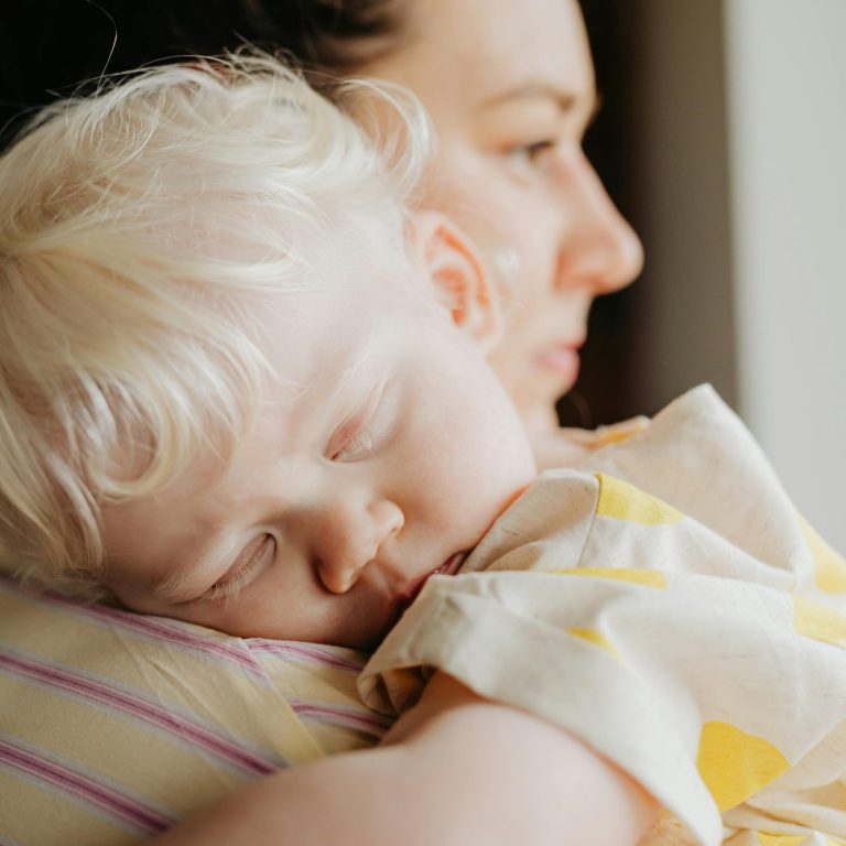 Een vrouw houdt een slapende dreumes in haar armen, beiden met serene gezichten.