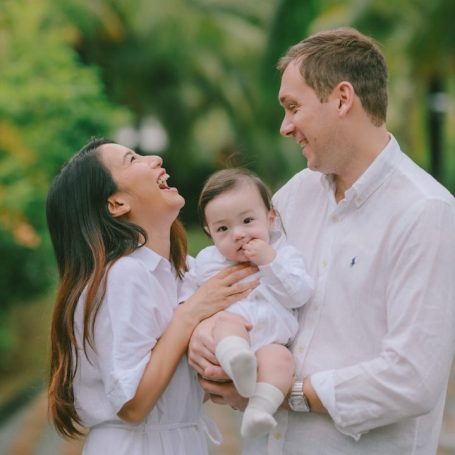 Gelukkige ouders houden hun baby vast, omringd door groene planten.